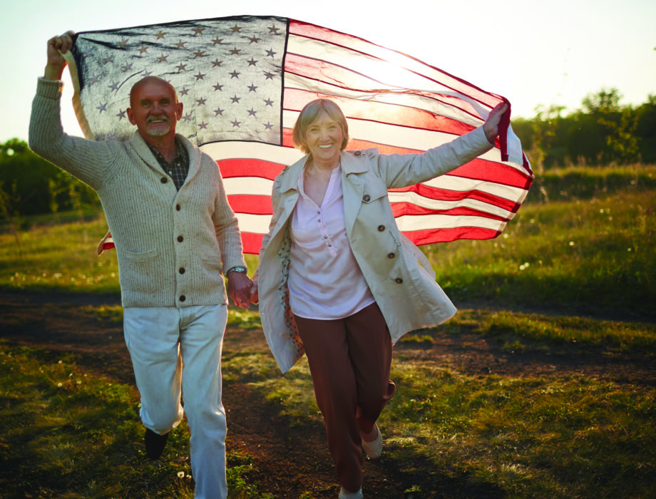 Two people walking outdoors holding a large American flag, symbolizing patriotism and honoring Veterans.