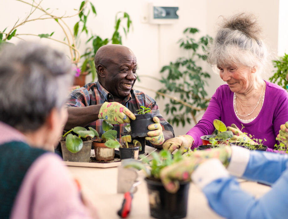 Older adults smiling and planting small potted plants together during a spring gardening activity indoors.